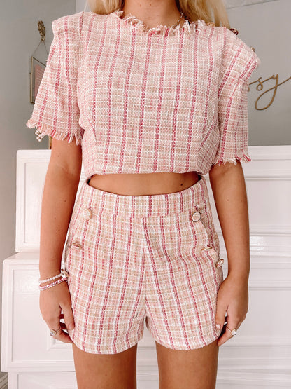 Pink and beige tweed shorts with gold buttons, shown on a model.
