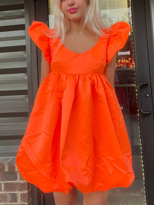 Bright orange mini dress with puff sleeves, shown on a model outdoors.
