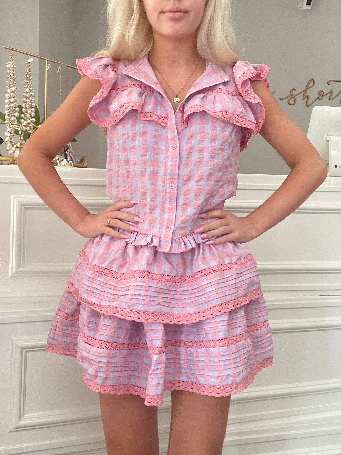 Pink gingham mini skirt with tiered ruffles and delicate lace trim, modeled against a white backdrop.
