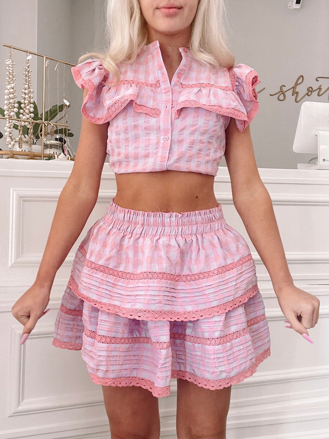 Pink gingham mini skirt with tiered ruffles and delicate lace trim, shown on a model.
