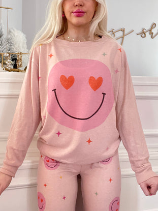 Pink pajama set featuring a smiley face design; long sleeves and pants with playful hearts and stars.
