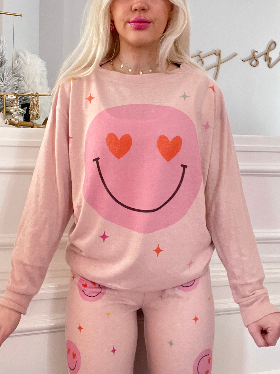 Pink pajama set featuring a smiley face design; long sleeves and pants with playful hearts and stars.
