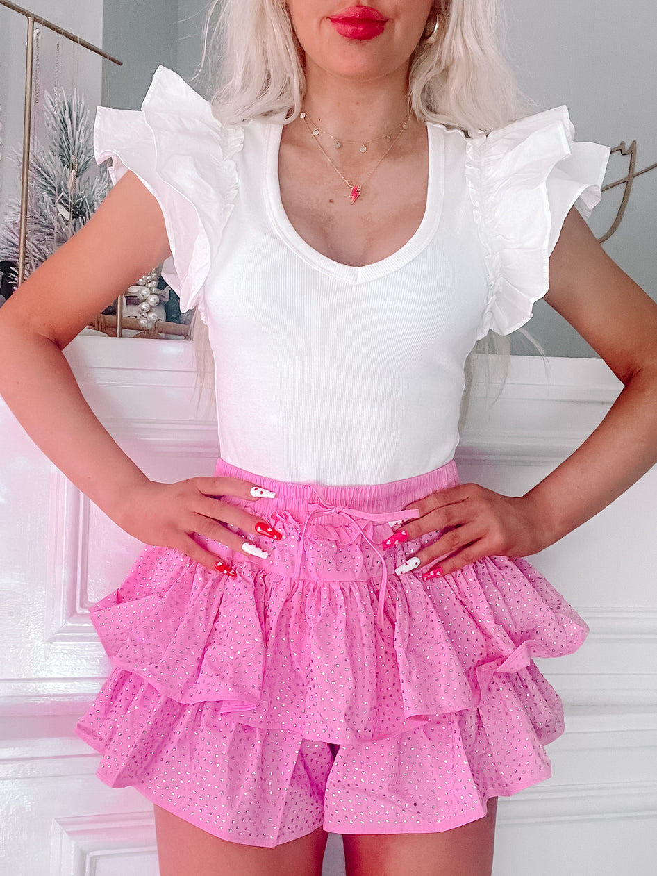Pink rhinestone mini skirt with tiered ruffles, styled with a white top.
