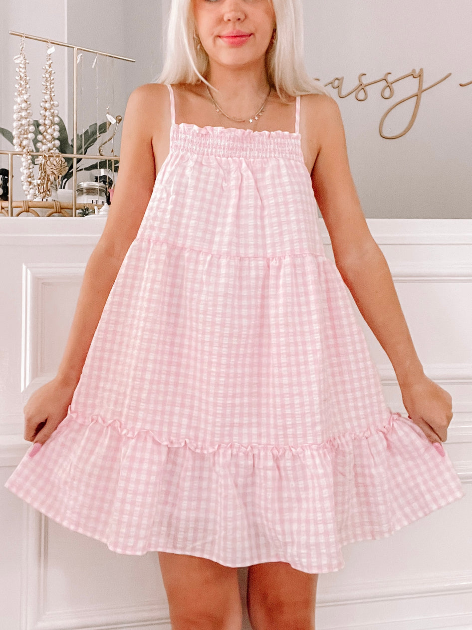 Pink gingham mini dress with tiered ruffle hem, shown on a model.
