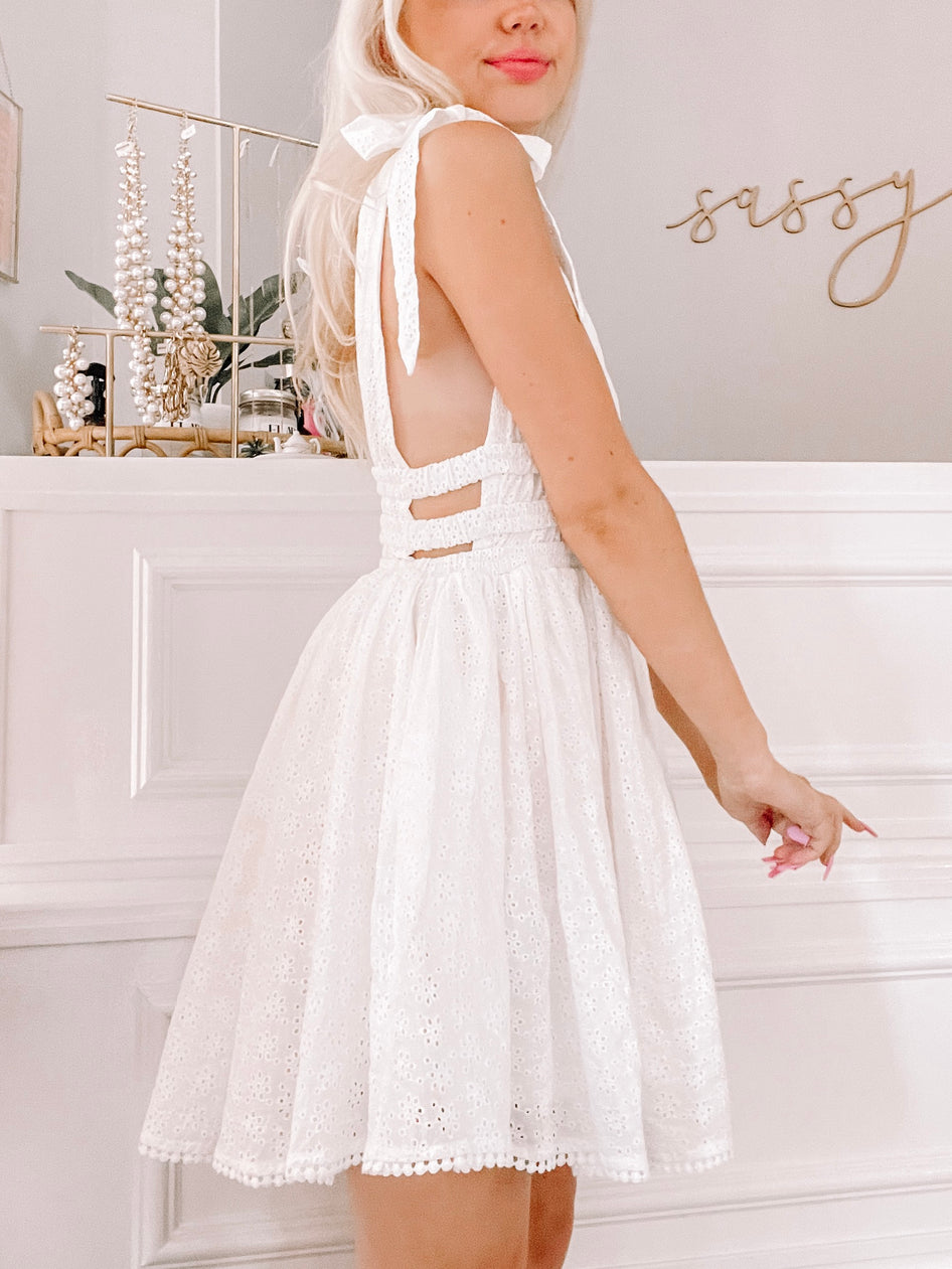 White eyelet mini dress with tie straps, shown against a white background.
