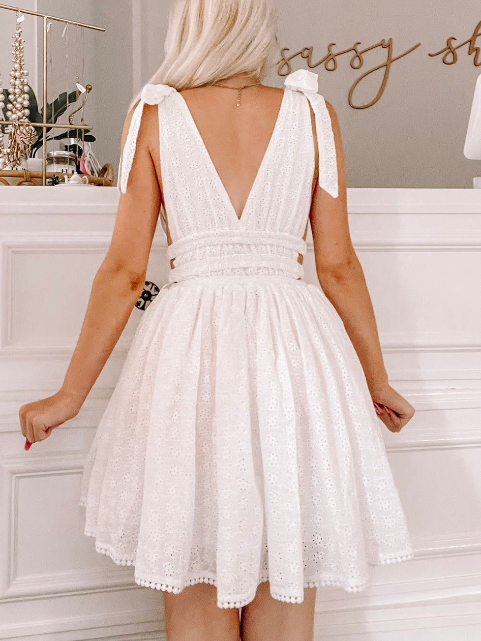 White eyelet dress with a fitted bodice and a flowy skirt, featuring delicate eyelet detailing and cute tie straps.
