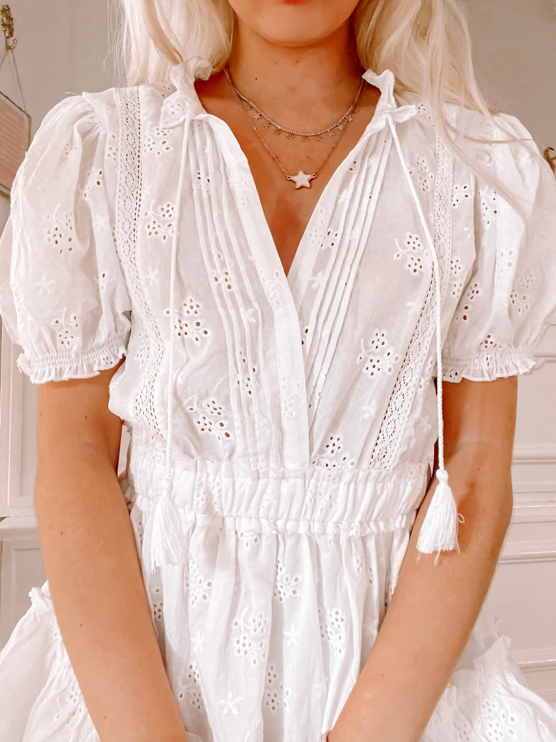 White eyelet mini dress with puff sleeves and drawstring waist, detailed embroidery.
