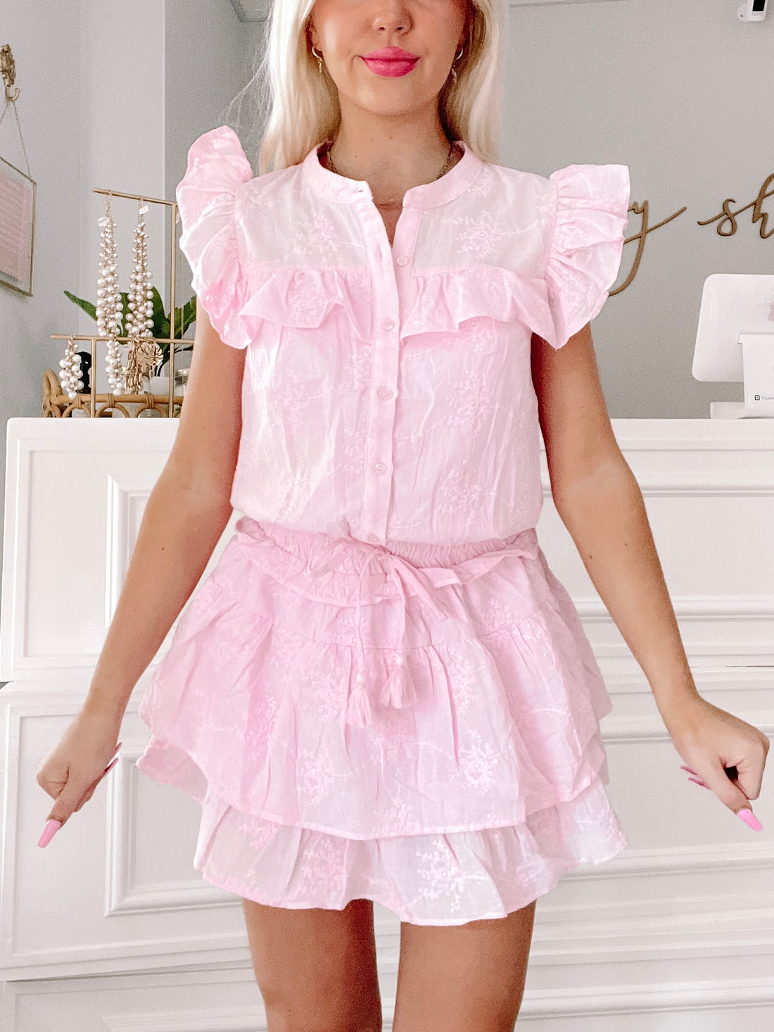 Pink embroidered eyelet dress with ruffle detailing and a tiered skirt, shown on a model.
