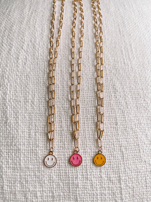 Gold chain necklaces with colorful smiley face charms on a textured white background.
