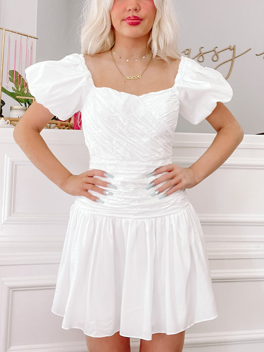 White puff-sleeve mini dress with a fitted bodice and gathered skirt, shown on a model.