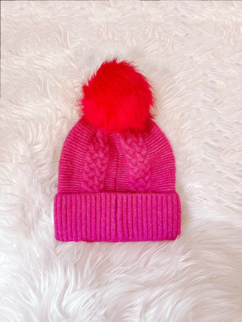 Pink cable knit beanie with red pompom
