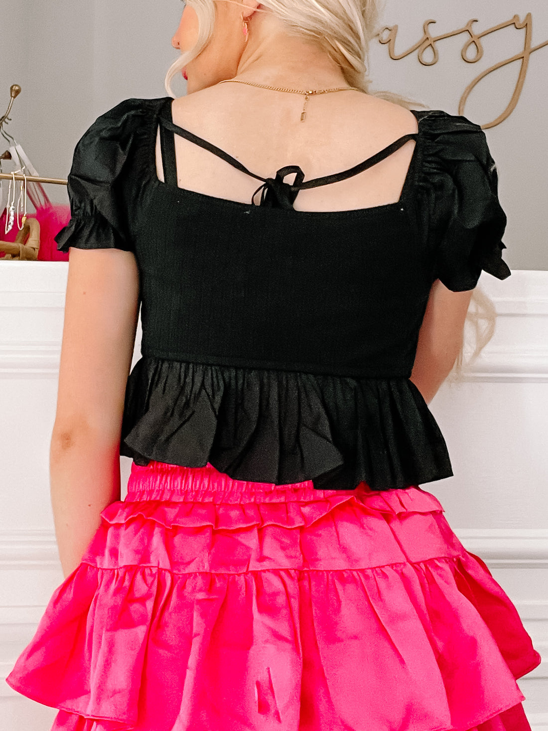 Black puff-sleeve crop top with tie back detail, shown paired with a hot pink skirt.
