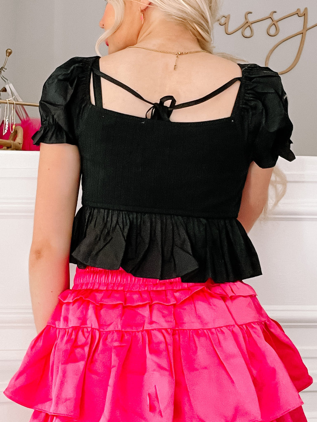 Black puff-sleeve crop top with tie back detail, shown paired with a hot pink skirt.
