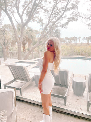 White ruffle mini dress, showcased near a poolside patio with lush greenery.
