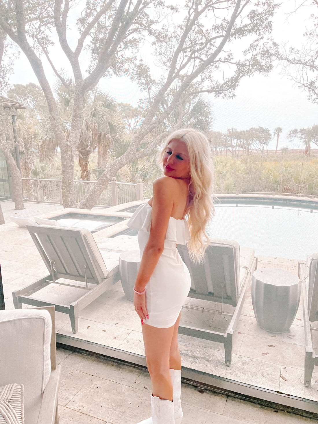 White ruffle mini dress, showcased near a poolside patio with lush greenery.
