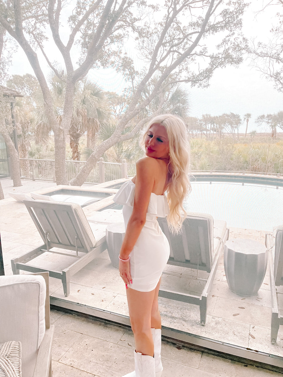 White ruffle mini dress, shown on model near a pool;  outdoor setting.
