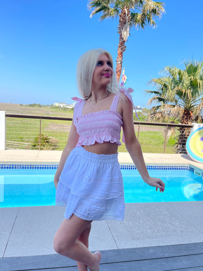 Woman by pool in pink crop top and white eyelet skirt.
