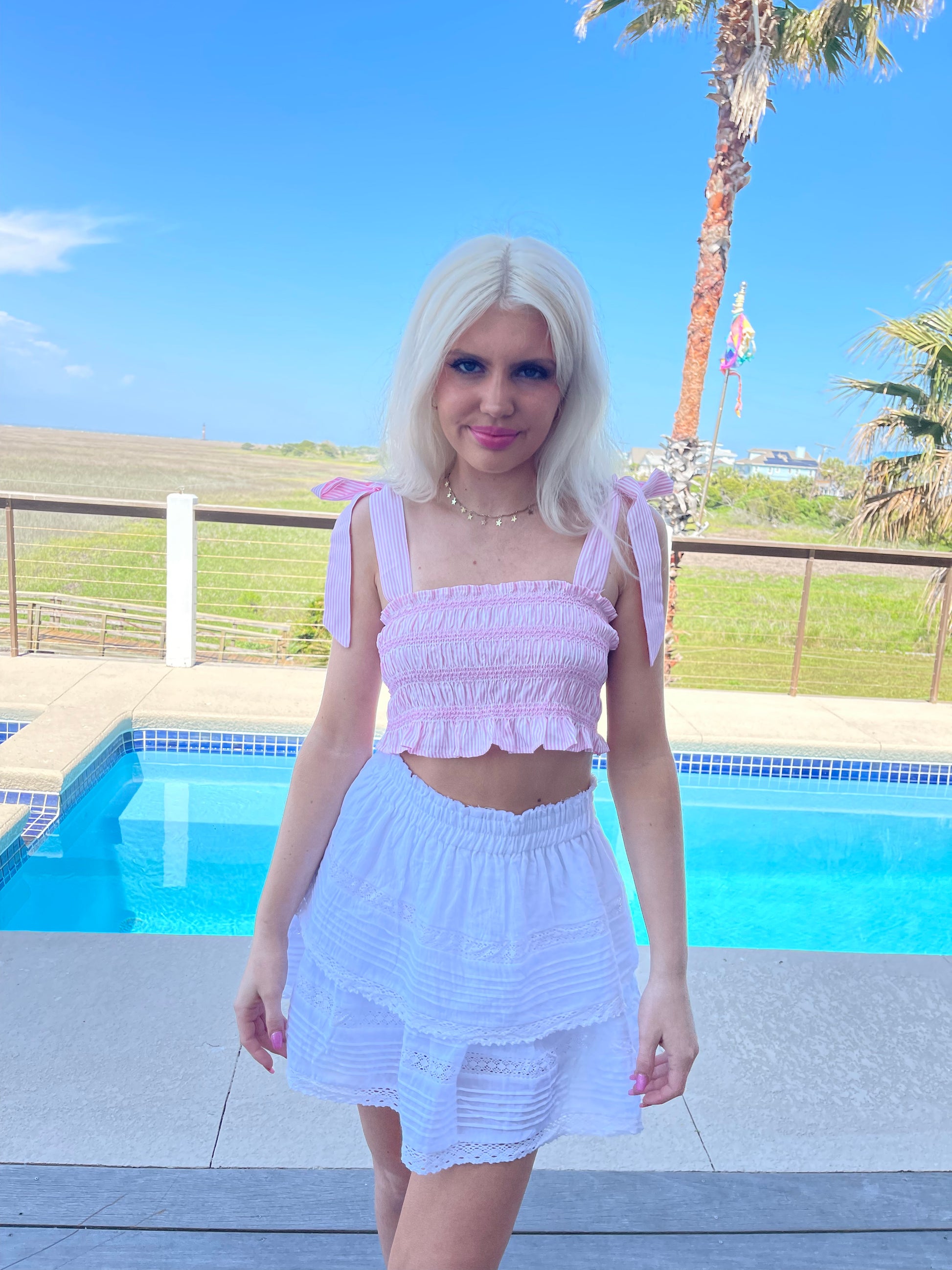 Pink striped crop top and white eyelet skirt, poolside summer fashion.
