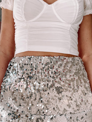 Sparkly silver sequined mini skirt paired with a white fitted top.
