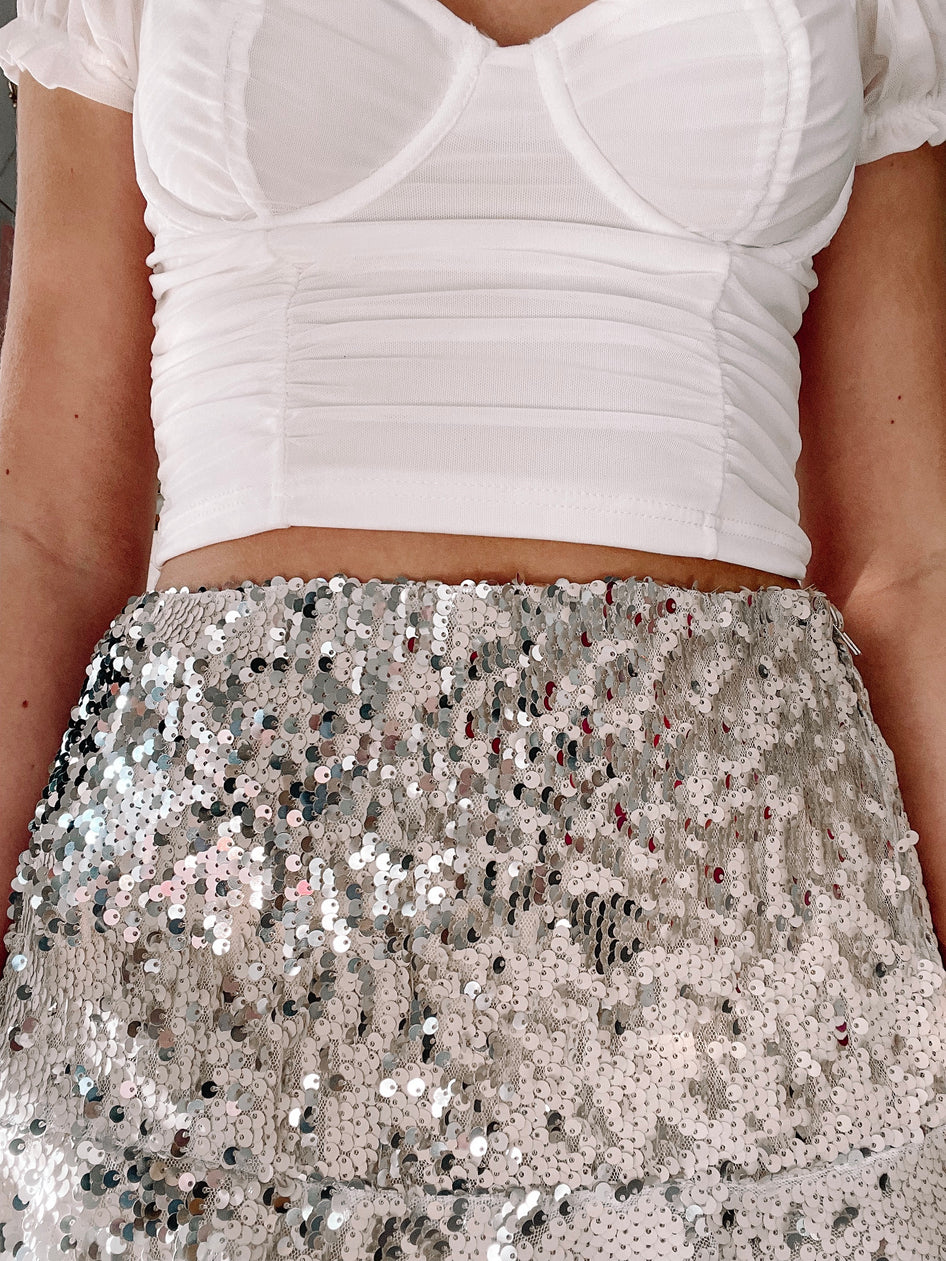 Sparkly silver sequined mini skirt paired with a white fitted top.
