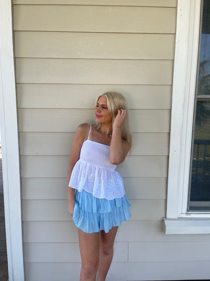 Sky blue tiered mini skirt; layered ruffle design, worn outdoors against light beige siding.
