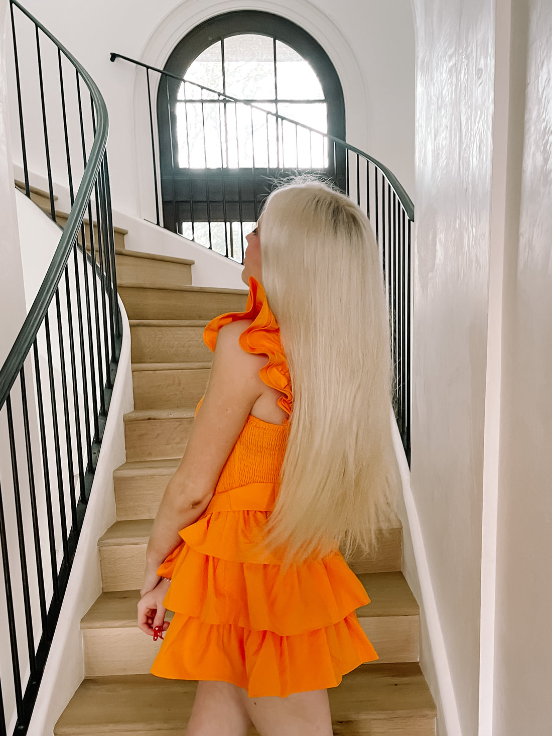 Bright orange tiered mini dress on a model ascending a wooden staircase.
