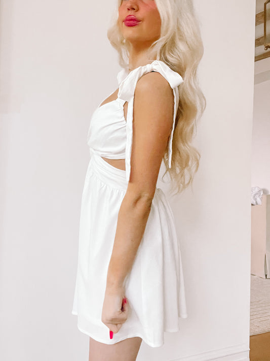 White mini dress with cut-out sides and tie straps, shown on a model against a light background.