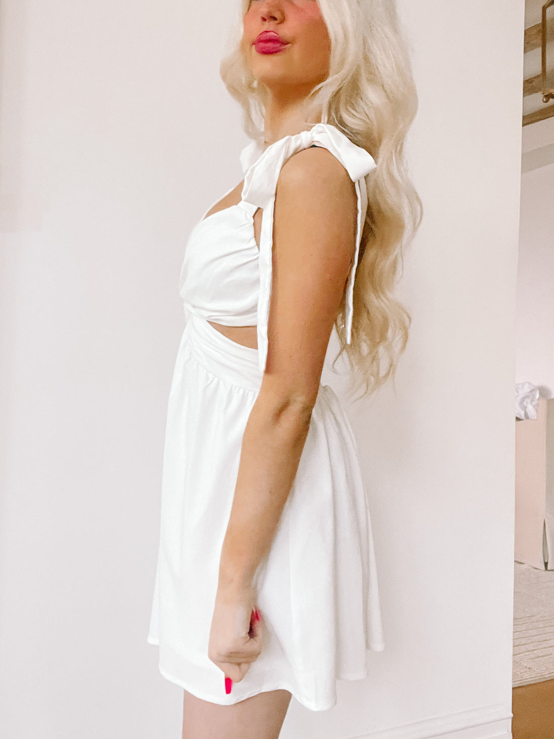 White mini dress with cut-out sides and tie straps, shown on a model against a light background.
