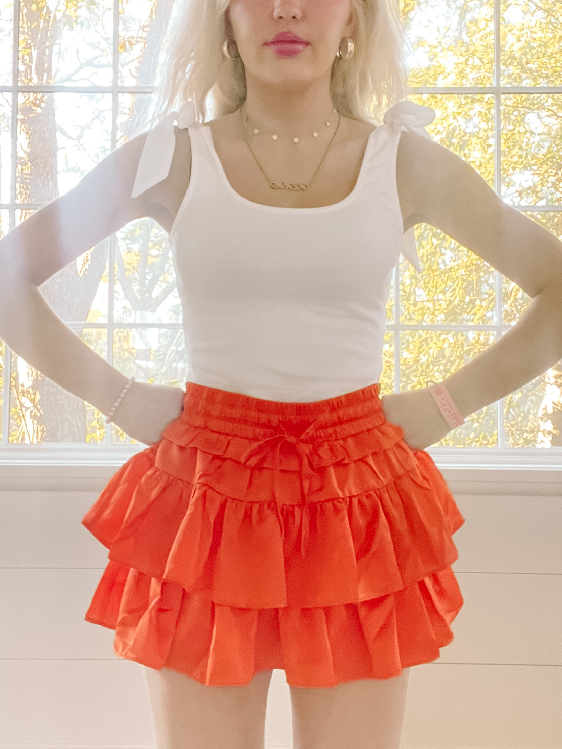 Orange tiered ruffle mini skirt styled with a white tank top, near a window.
