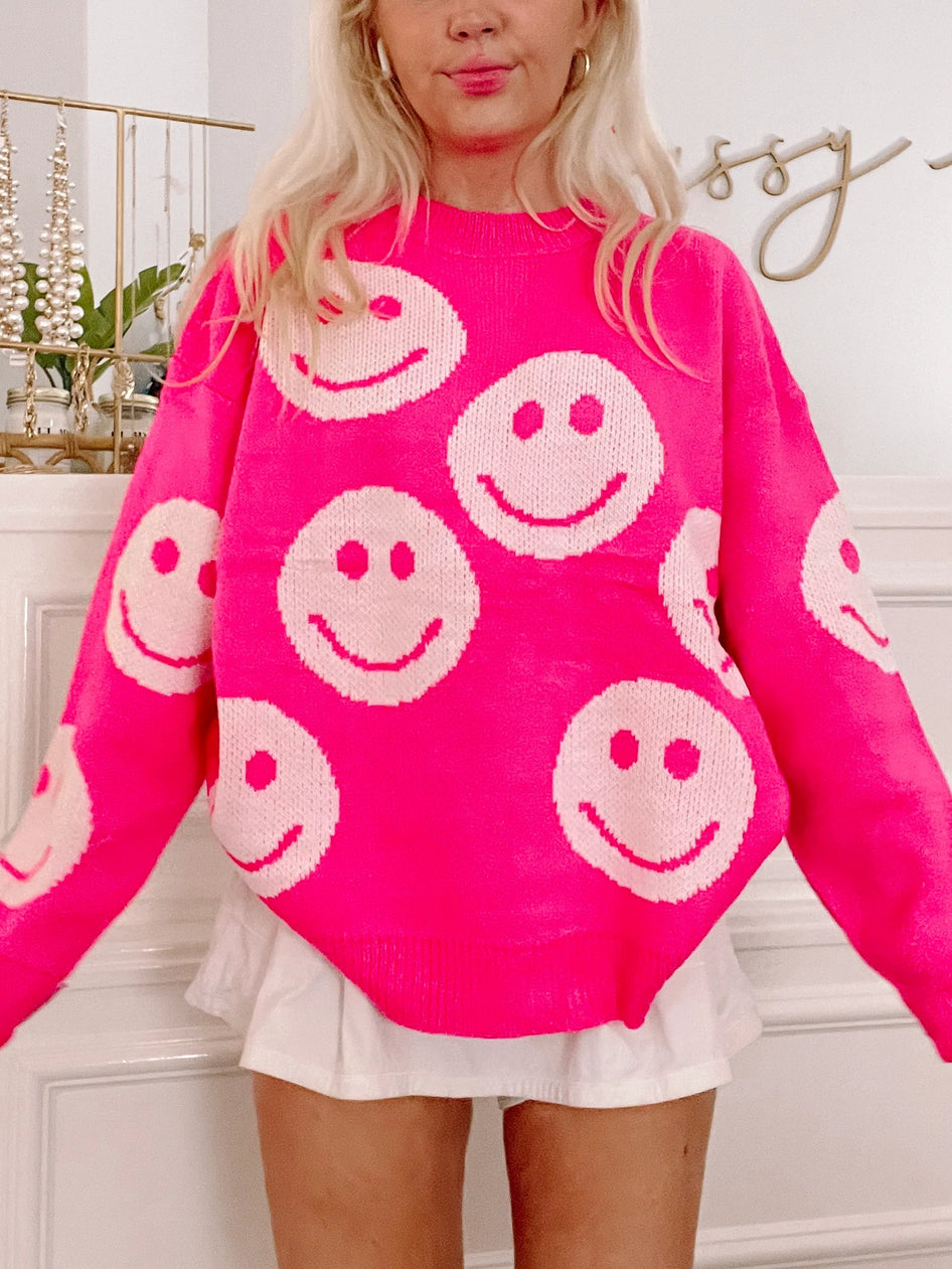 Hot pink knit sweater adorned with playful cream-colored smiley faces.
