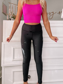 Black star-print leggings styled with a pink top, shown against a white dresser.
