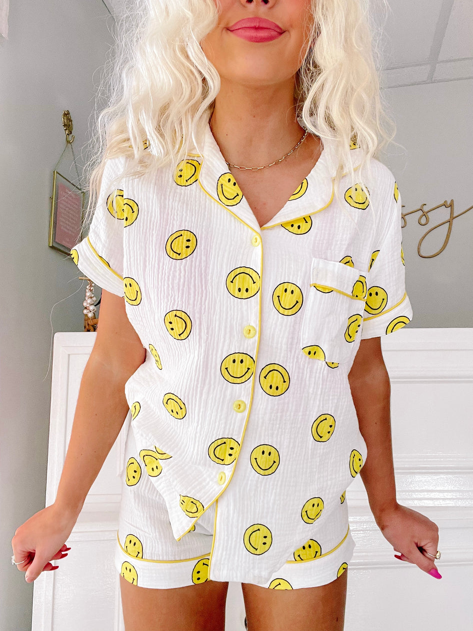 White short pajama set with yellow smiley faces, modeled on a person.
