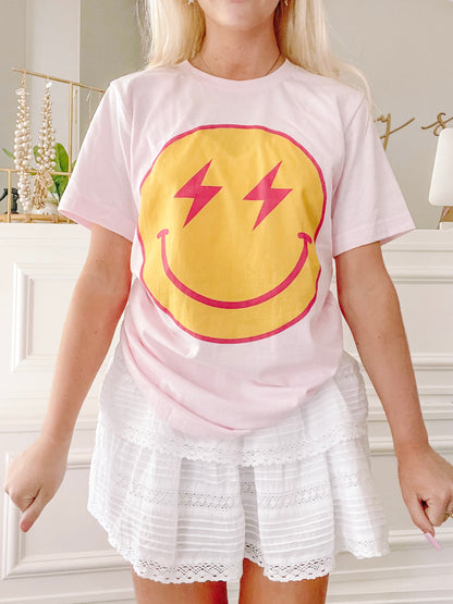 Pink Striking Smiles tee featuring a yellow smiley face with pink lightning bolts.
