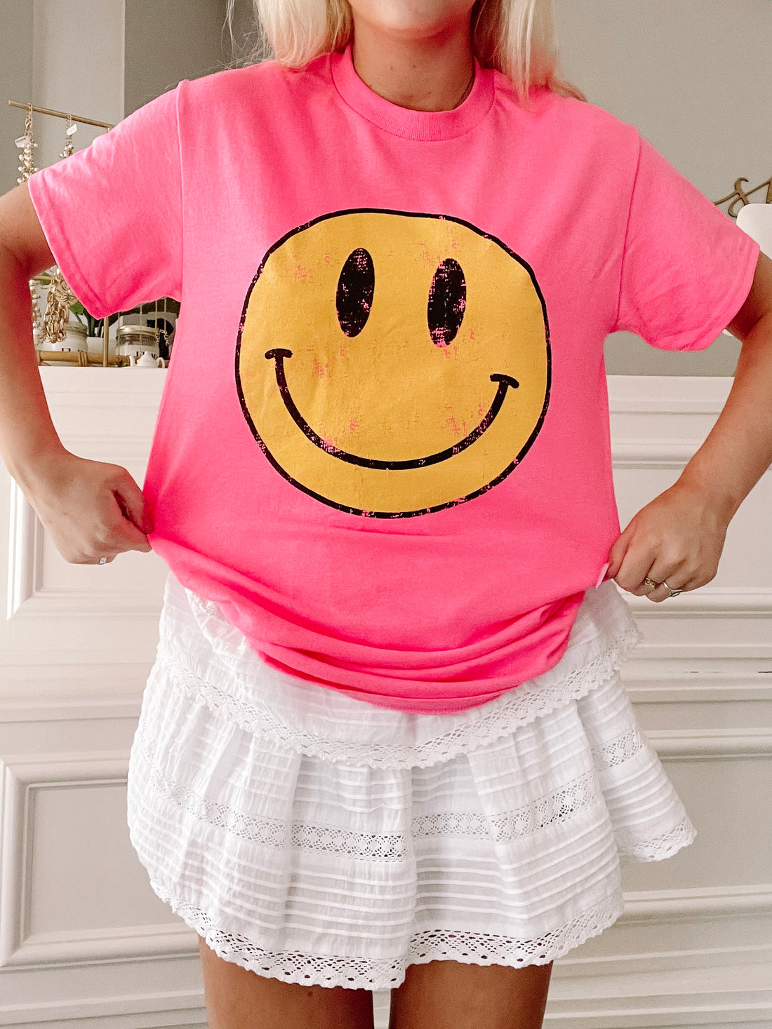 Hot pink tee showcasing a vintage-style yellow smiley face, modeled with a white eyelet skirt.
