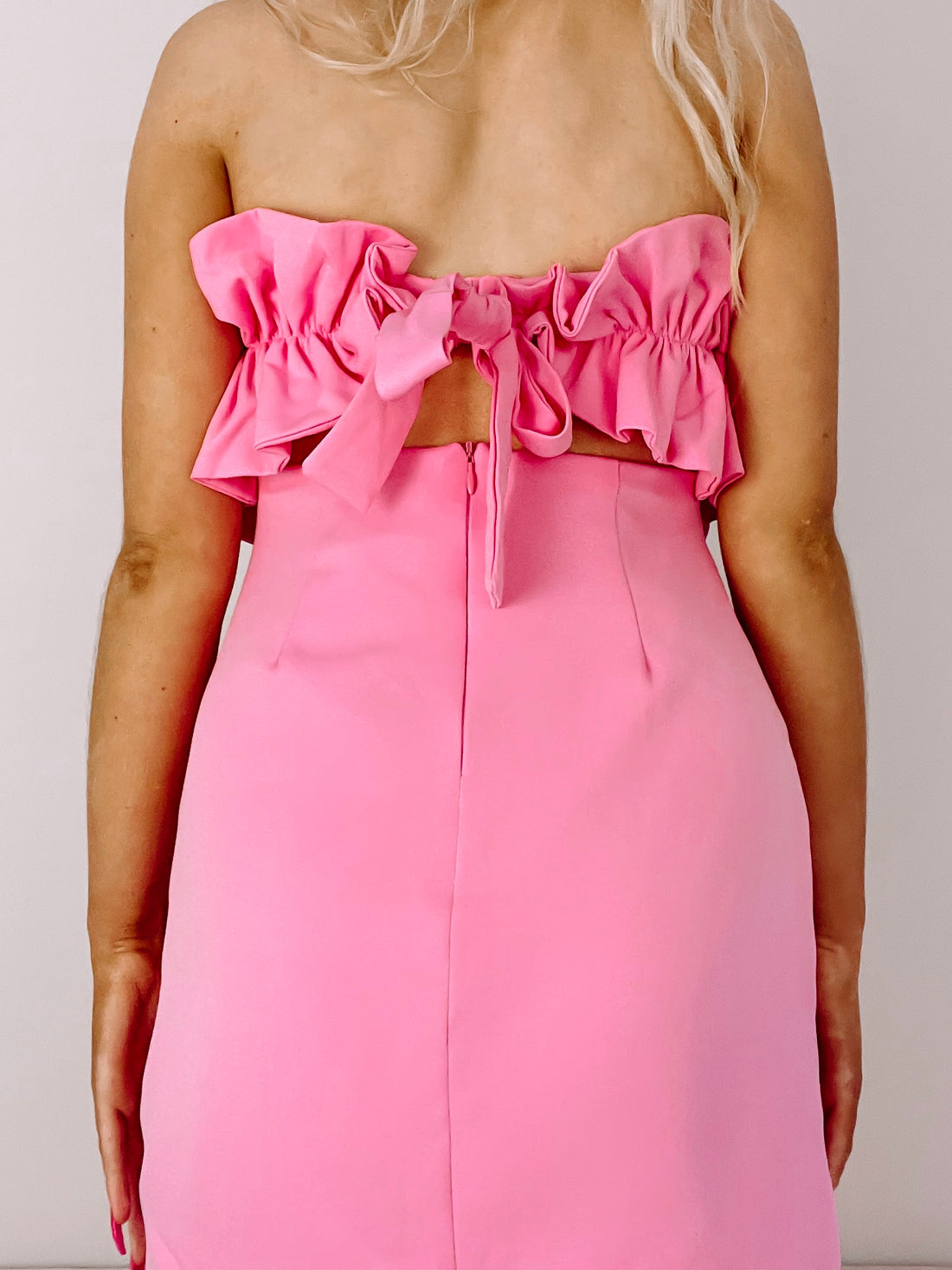 Pink mini dress with ruffled bodice and tie back detail.
