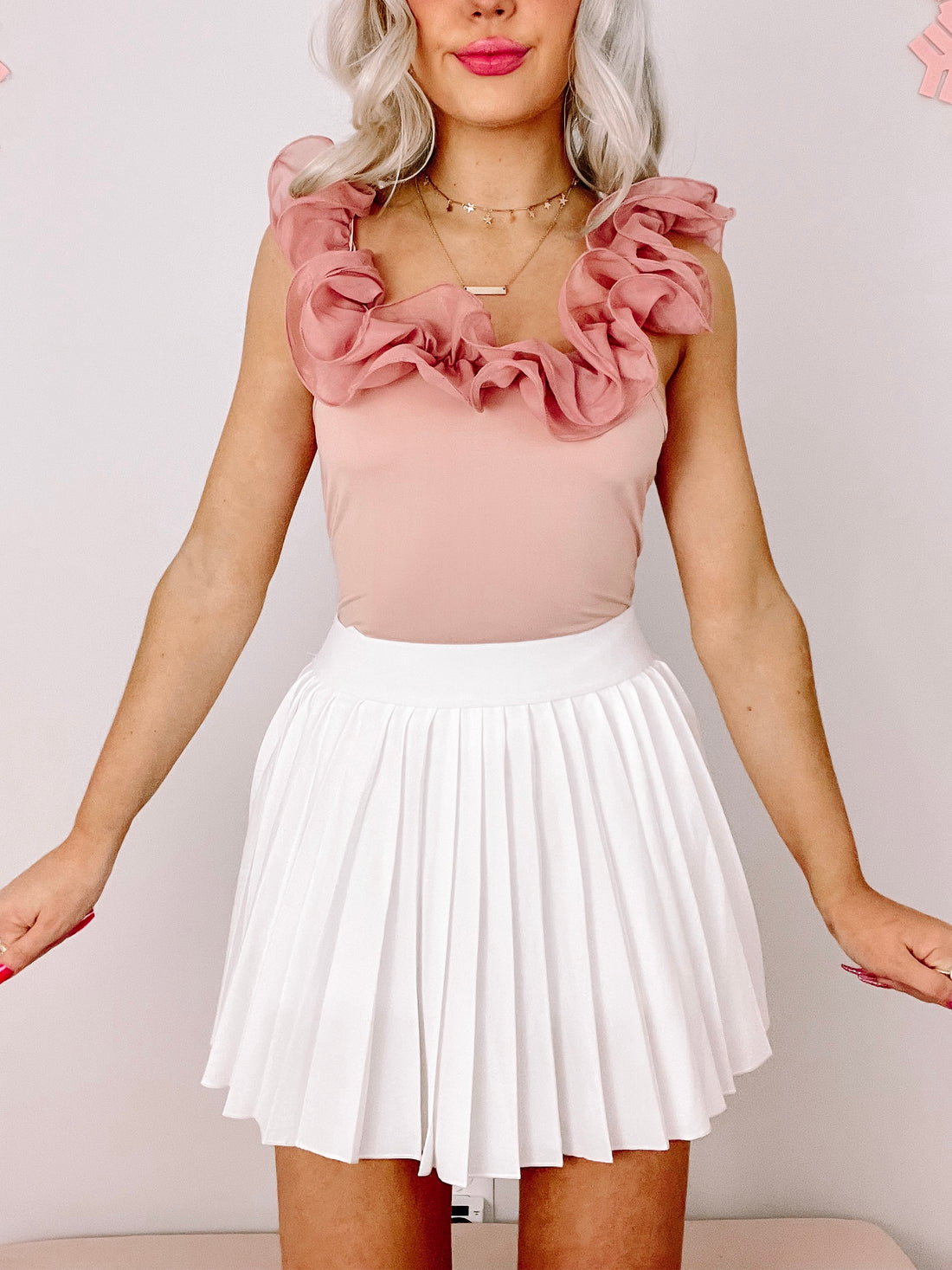 Dusty rose ruffle bodysuit paired with a white pleated mini skirt.
