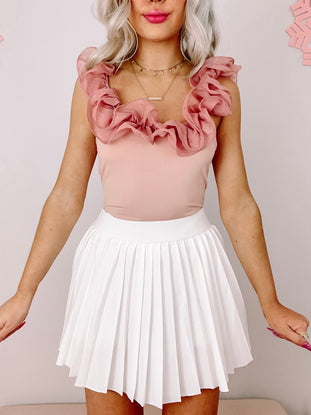 Lennox Ruffle Bodysuit: Dusty rose bodysuit with ruffled neckline, paired with white pleated tennis skirt.
