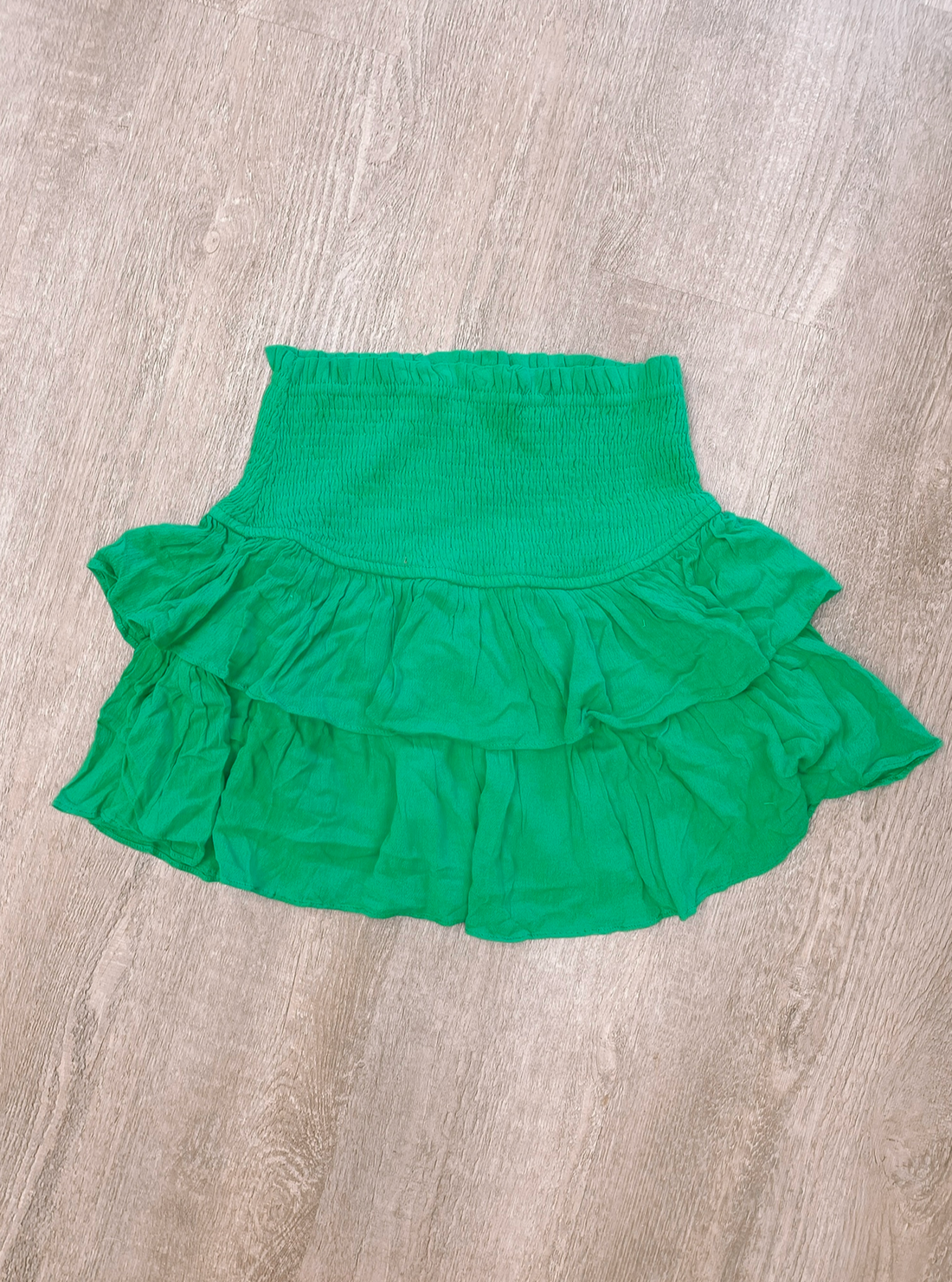 Kelly green tiered mini skirt, smocked waistband, displayed on wood surface.
