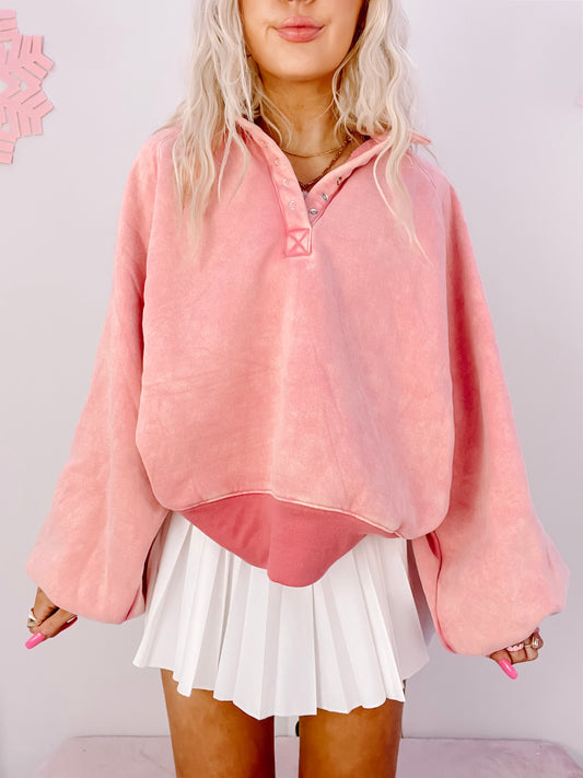Pink pullover sweater with button detail, modeled with white pleated skirt.