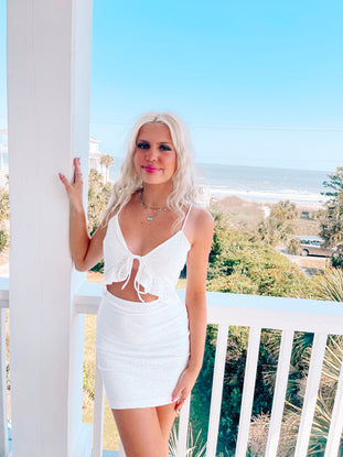 White eyelet mini dress on a beachside porch.
