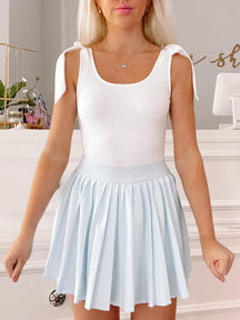White Brynn bodysuit with tie straps and light blue pleated mini skirt.
