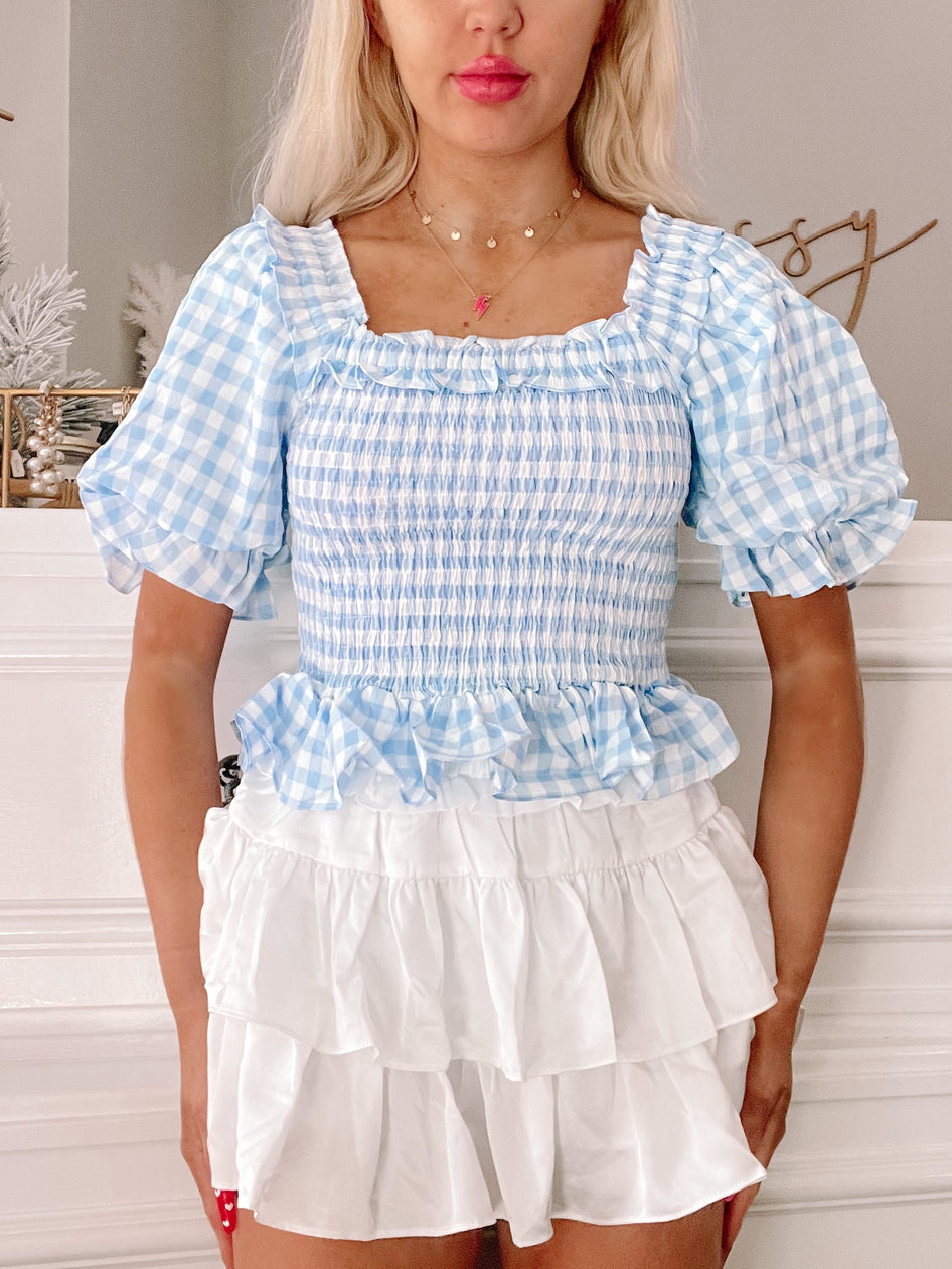 Blue gingham puff-sleeve top with smocked bodice, paired with a layered white ruffle skirt.
