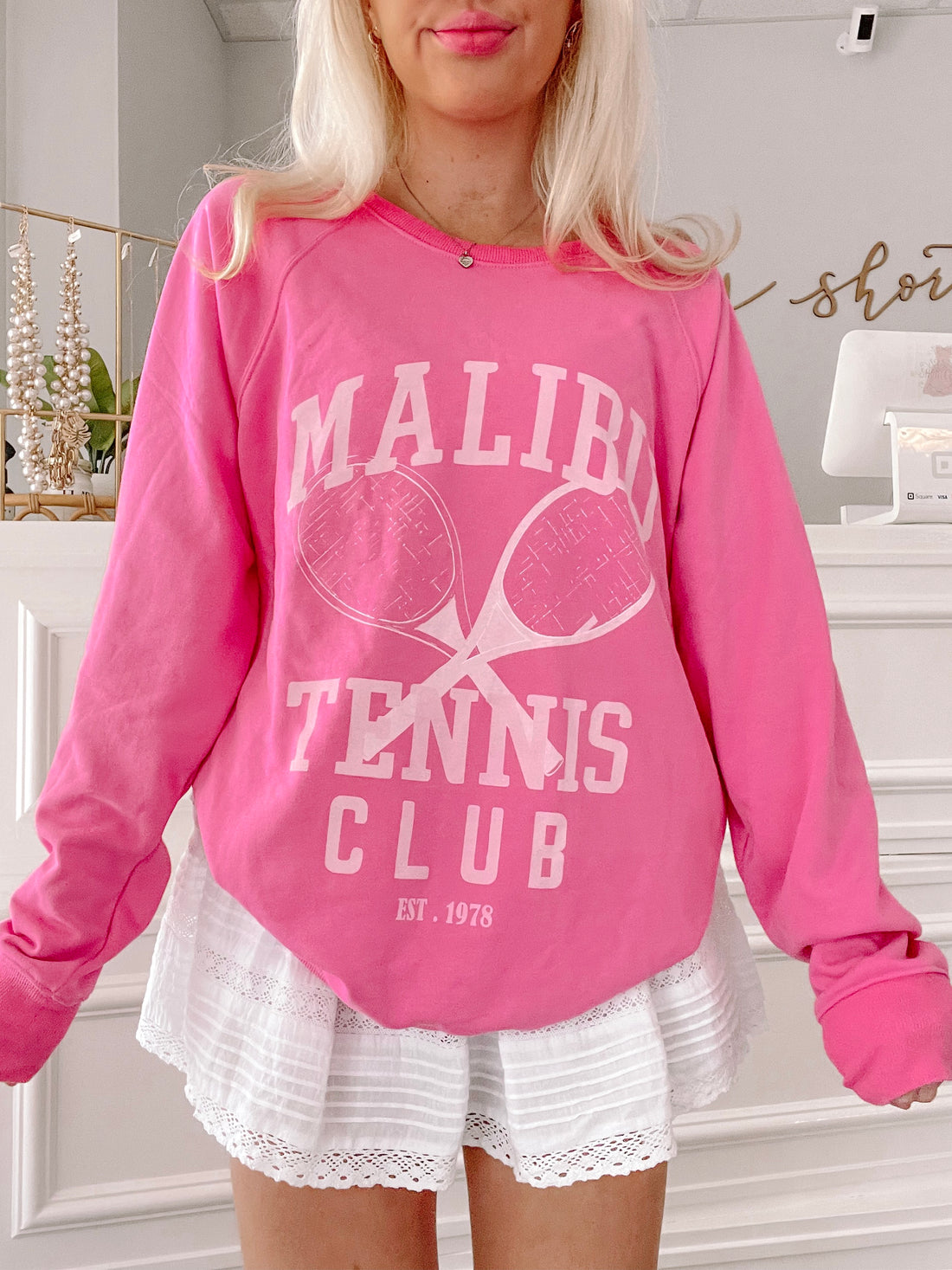 Hot pink crewneck sweatshirt with tennis-themed graphic; styled with white eyelet shorts.
