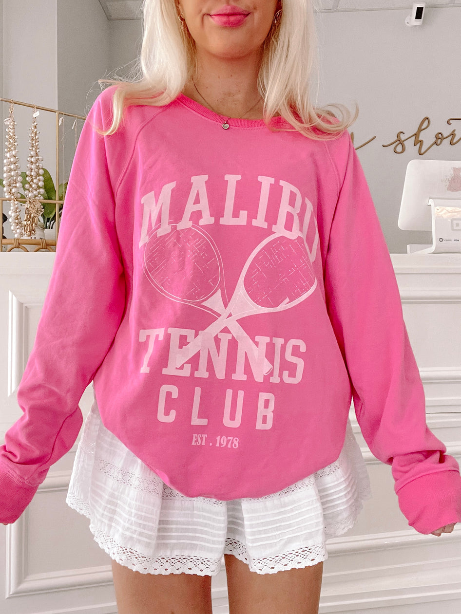 Hot pink crewneck sweatshirt with tennis-themed graphic; styled with white eyelet shorts.
