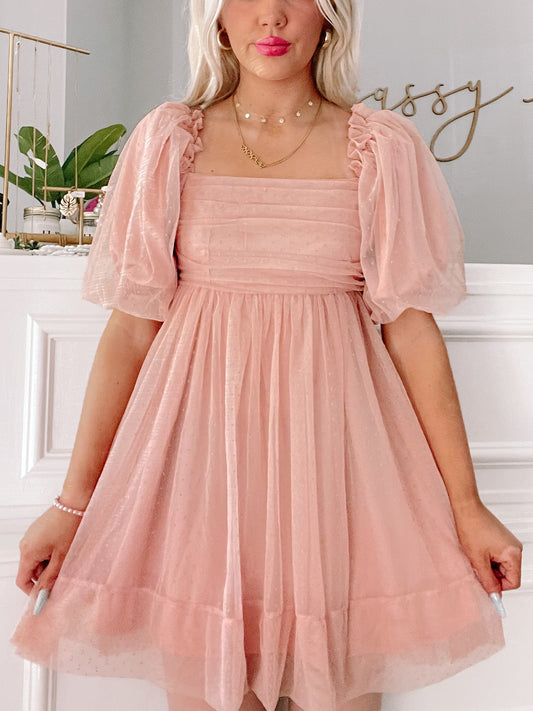 Blush pink mini dress with puff sleeves; delicate fabric, fit-and-flare silhouette.