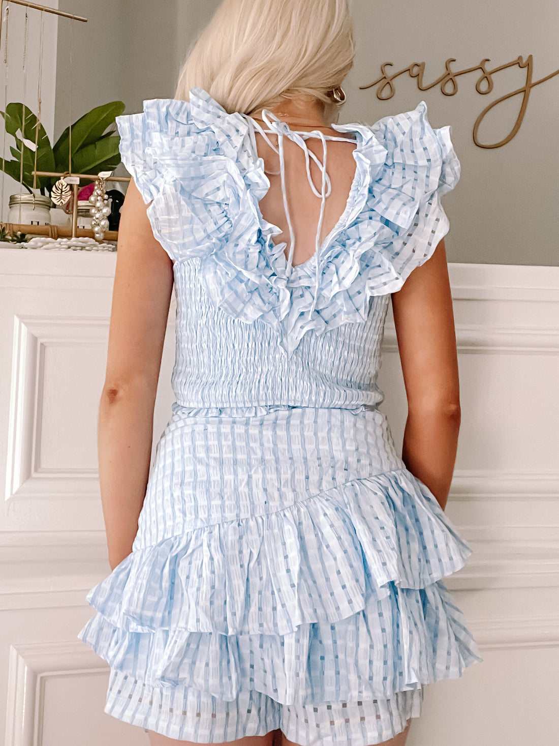 Light blue eyelet mini dress with ruffled layers, shown from the back against a white wall.
