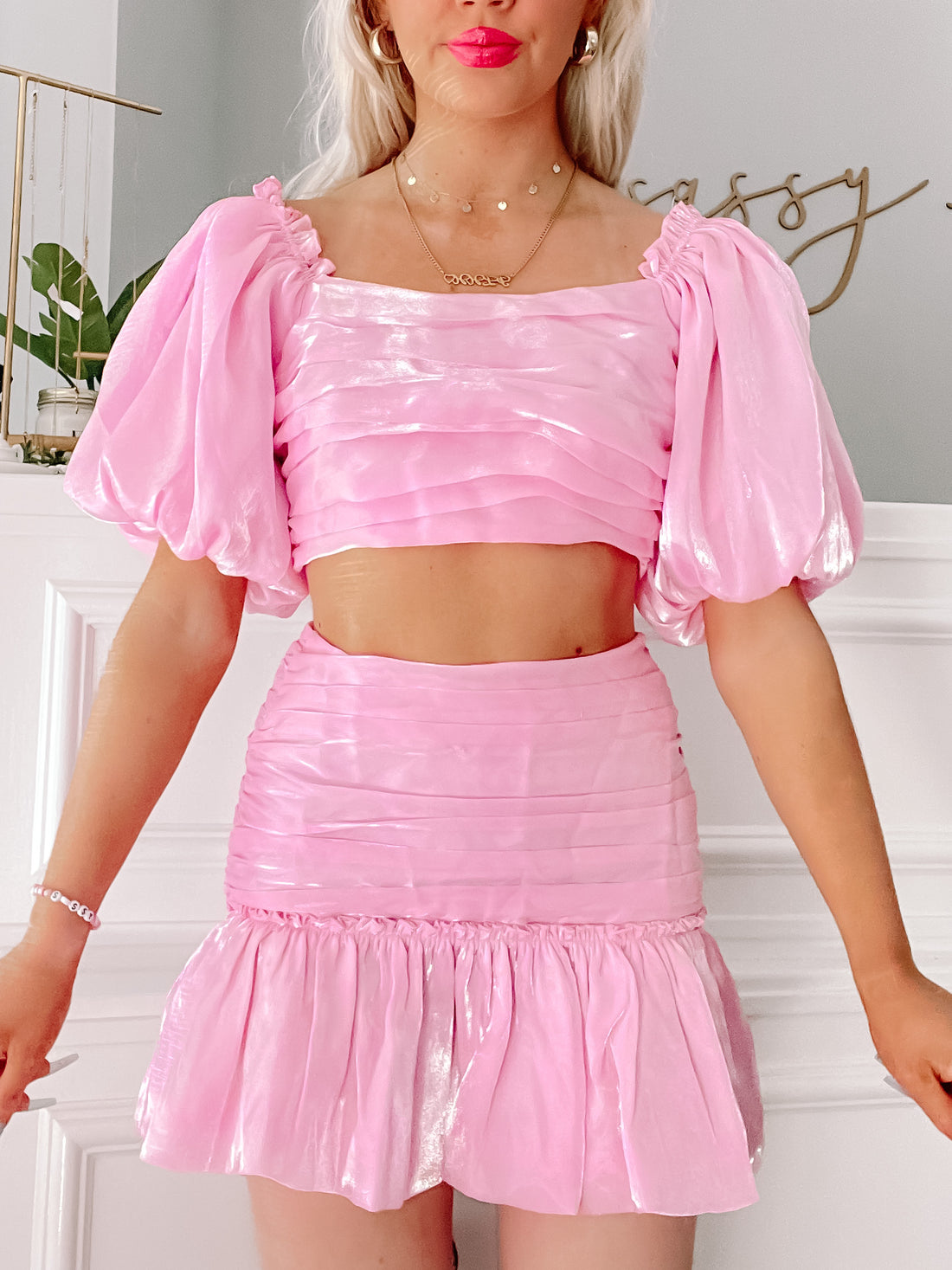 Pink satin two-piece outfit: cropped puff-sleeve top and ruffled mini skirt.
