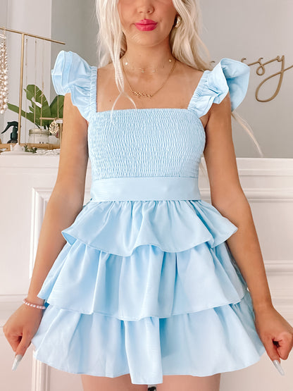 Light blue tiered mini dress with ruffle sleeves, shown on a model against a neutral background.
