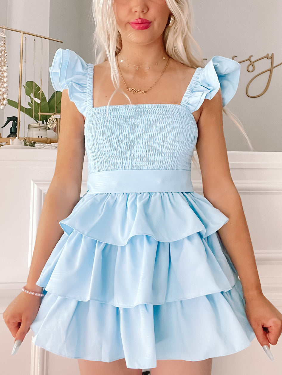 Light blue tiered mini dress with ruffle sleeves, shown on a model against a neutral background.
