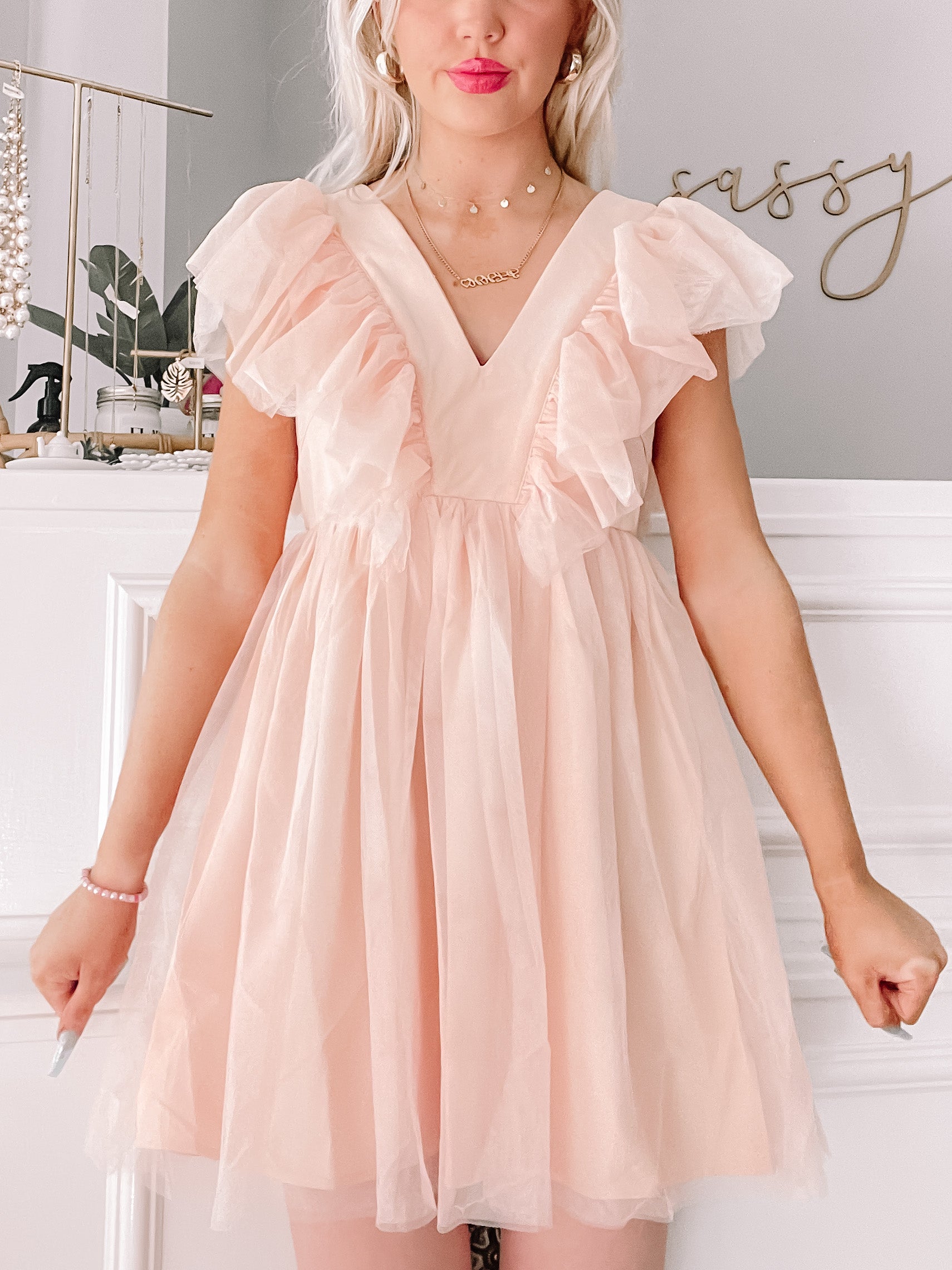 Blush pink tulle dress with ruffled sleeves, shown on a model against a white wall.
